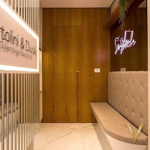 Recepção de clínica odontológica com parede em lâmina natural, ripado vertical e banco de espera estofado