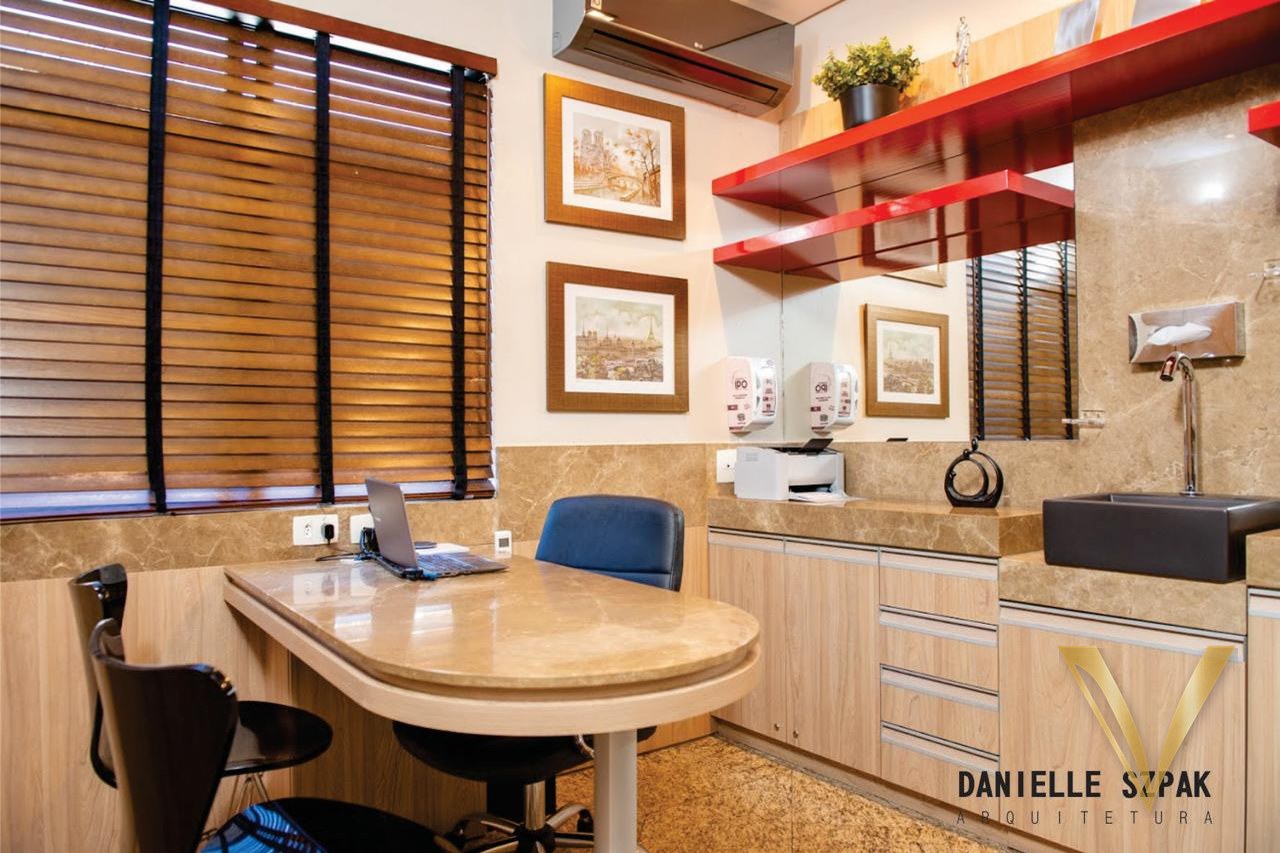 Sala de atendimento com mesa curva em pedra, prateleiras vermelhas e bancada com cuba