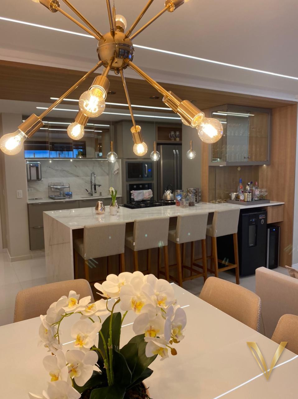 Sala de jantar com lustre dourado e vista para a cozinha sob medida